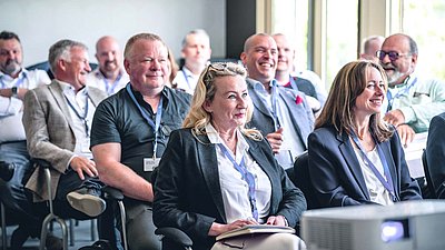Conference attendees sit attentively and smiling in the audience during a presentation