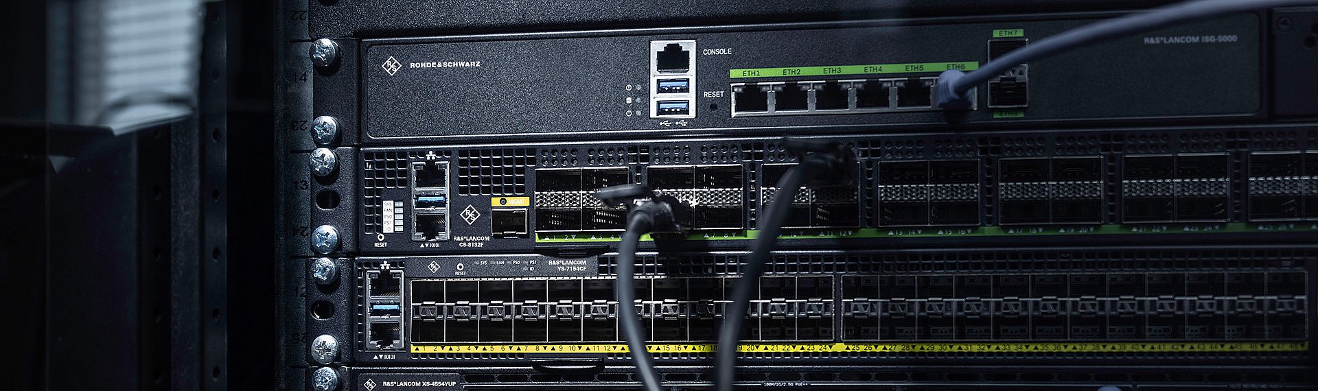 Three R&S®LANCOM Switches installed in the rack with cables: core switch R&S®LANCOM CS-8132F, aggregation switch R&S®LANCOM YS-7154CF, and access switch R&S®LANCOM XS-4554XUP