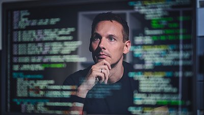 Man studies programming code on multiple computer screens.