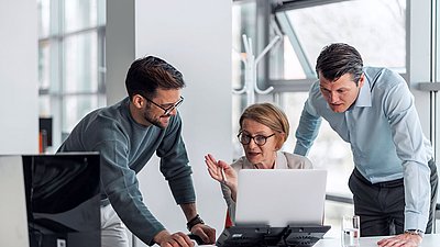 Groupe de trois employés de l’administration publique assis dans un bureau, en concertation autour d’un ordinateur portable