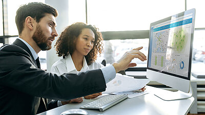 Two employees look at a monitor showing the R&S®LANCOM Management Cloud