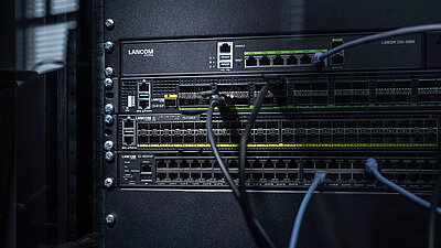 Three R&S®LANCOM Switches installed in the rack with cables: core switch R&S®LANCOM CS-8132F, aggregation switch R&S®LANCOM YS-7154CF, and access switch R&S®LANCOM XS-4554XUP