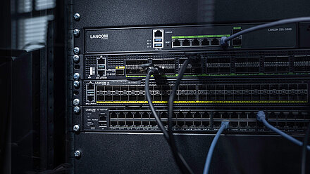 Three R&S®LANCOM Switches installed in the rack with cables: core switch R&S®LANCOM CS-8132F, aggregation switch R&S®LANCOM YS-7154CF, and access switch R&S®LANCOM XS-4554XUP