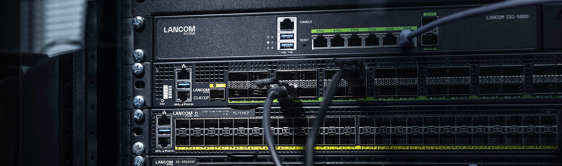 Three R&S®LANCOM Switches installed in the rack with cables: core switch R&S®LANCOM CS-8132F, aggregation switch R&S®LANCOM YS-7154CF, and access switch R&S®LANCOM XS-4554XUP